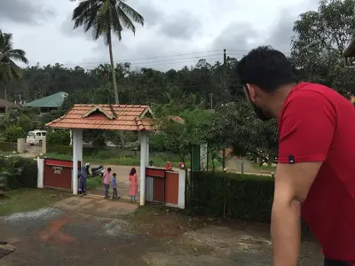a man in a red shirt standing next to a small building at Marsim Holiday Resort in Vythiri