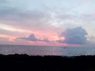 a sunset over the ocean with a rock wall at Liberty House - SeaView in Kozhikode