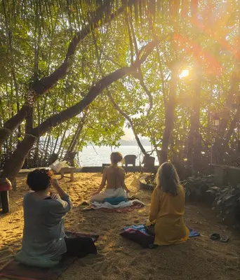 a group of people sitting on the beach under a tree at Lakefront Beach Homes in Cherai Beach