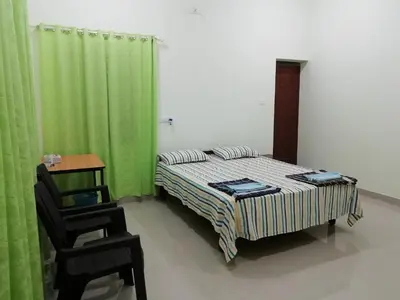 a bedroom with a bed and a chair and green curtains at Kannur west beach homestay in Kannur