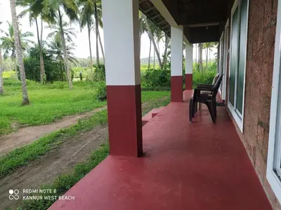 a porch of a house with a red floor and chairs at Kannur west beach homestay in Kannur