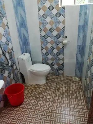 a bathroom with a toilet and a red bucket at Kannur west beach homestay in Kannur