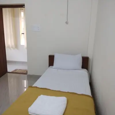 a small bedroom with a bed with a yellow blanket at Manjira Lodge in Guruvāyūr