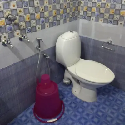 a bathroom with a toilet and a red bucket at Manjira Lodge in Guruvāyūr