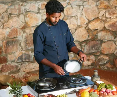 a man is preparing food on a stove at Raindrops Resorts Wayanad in Sultan Bathery