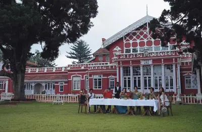 a group of people sitting at a table in front of a red building at WelcomHeritage Fernhills Royal Palace in Ooty