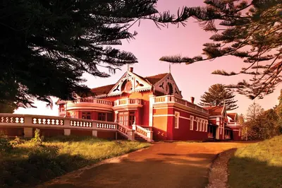 a large red house with a driveway in front at WelcomHeritage Fernhills Royal Palace in Ooty