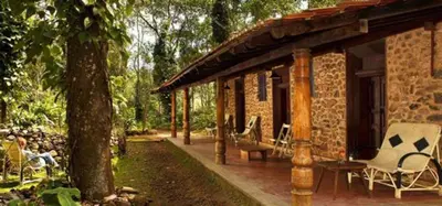 a brick house with a porch and chairs on a patio at Elephant Valley Eco Farm Hotel in Kodaikānāl