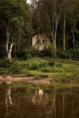 a house sitting next to a body of water at Elephant Valley Eco Farm Hotel in Kodaikānāl