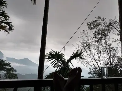 a person sitting on a balcony looking out at the mountains at The Hillock-quiet by the Mountains in Vallikavungal