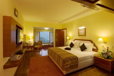 a hotel room with a large bed and a desk at Gem Park Ooty in Ooty