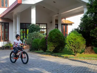 a young boy riding a bike in front of a building at Amritara Ambatty Greens Resort in Virajpet