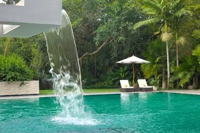 a fountain in a pool with two chairs and an umbrella at Amanvana Spa Resort, Coorg in Kushālnagar