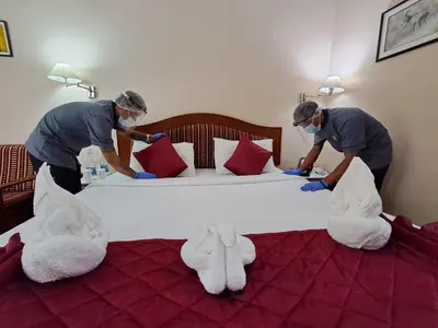 two men are making a bed with white towels at Hotel Preethi Classic Towers in Ooty