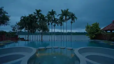 a swimming pool with a view of the water and palm trees at The River Retreat Heritage Ayurvedic Resort in Shoranūr