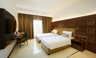a hotel room with two beds and a desk at Flora Airport Hotel and Convention Centre Kochi in Nedumbassery