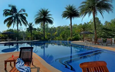 a swimming pool with two chairs and palm trees at Evolve Back Coorg in Siddapur