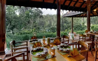 a dining room with a table and a large window at Evolve Back Coorg in Siddapur