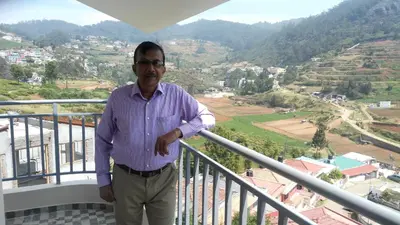 a man standing on a balcony overlooking a valley at Neo Nirmal Residency in Ooty