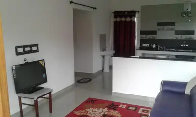 a living room with a tv and a couch and a kitchen at Neo Nirmal Residency in Ooty