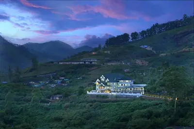 a building on a hill with mountains in the background at Elysium Garden in Munnar