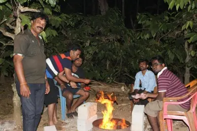 a group of men sitting around a fire pit at Dreams Home Estate Stay in Suntikoppa