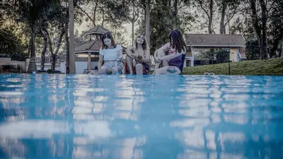 three girls sitting on the side of a swimming pool at Sandalo Castle Resorts in Gūdalūr