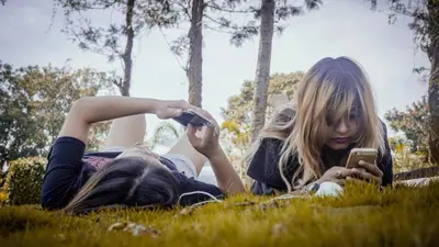 two girls laying on the grass looking at a cell phone at Sandalo Castle Resorts in Gūdalūr