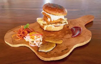 a sandwich on a wooden cutting board with chips and vegetables at Sixth Element in Kushālnagar