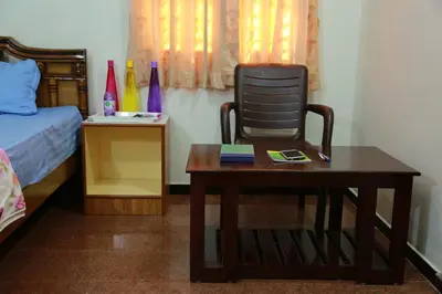 a bedroom with a chair and a table and a bed at Coimbatore Home Stay & Serviced Apartment in Coimbatore