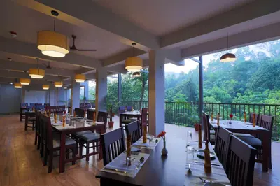 a restaurant with tables and chairs and a large window at Abad Brookside Wayanad in Vythiri
