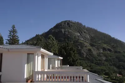 a white house with a mountain in the background at La Montana by TGI in Ooty