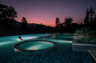 a woman is sitting in a swimming pool at sunset at Agraharam Resorts in Thirunelli