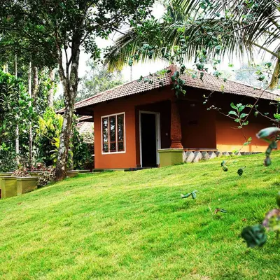 a small house on a grassy field in front of a house at Indeevara Luxury Resort and Spa, Wayanad in Vythiri