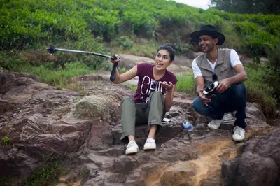 a man and a woman sitting on rocks with a camera at The Realm in Coonoor