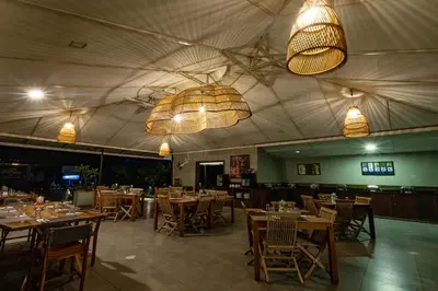 a restaurant with wooden tables and chairs and lights at Machaan Wilderness Lodge Nagarahole in Srimangala