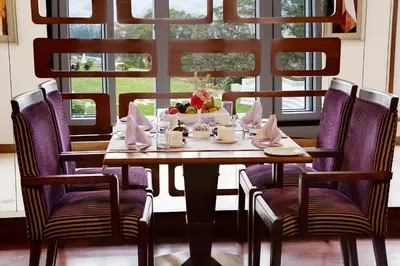 a table with purple chairs and a table with a bowl of fruit at Sinclairs Retreat Ooty in Ooty