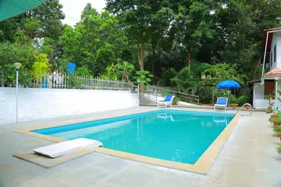 a swimming pool with two chairs and an umbrella at Ayuryogashram Heritage in Trichūr