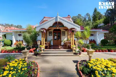 a house with a porch and flowers in front of it at Greenwood Bungalow Heritage In the heart of Ooty in Ooty