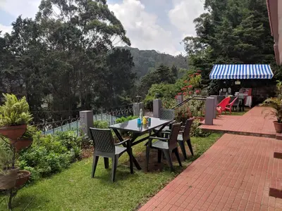 a patio with a table and chairs on the grass at REFLECTIONS Guest House in Ooty
