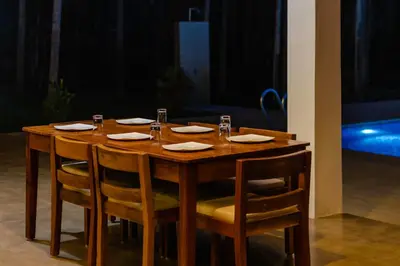 a wooden table with chairs and plates and glasses on it at StayVista at Tall Silver with Infinity Pool & Breakfast -2BR in Madikeri