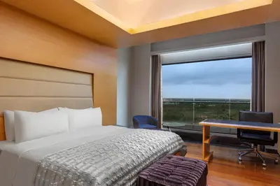 a bedroom with a bed and a desk and a window at Le Meridien Coimbatore in Coimbatore