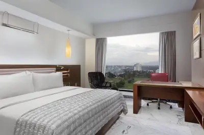a hotel room with a bed and a desk and a window at Le Meridien Coimbatore in Coimbatore