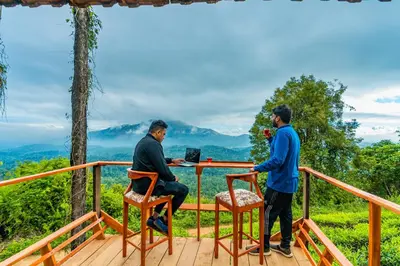 two men sitting at a table on a deck with a laptop at Zostel Plus Wayanad in Kalpetta
