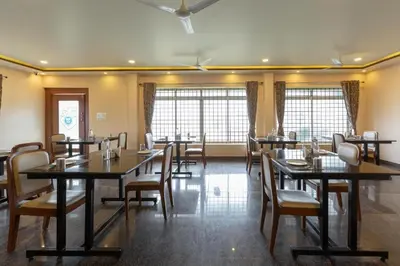 a dining room with tables and chairs and windows at KSTDC Hotel Mayura Biligiri, BR Hills in Honganūr