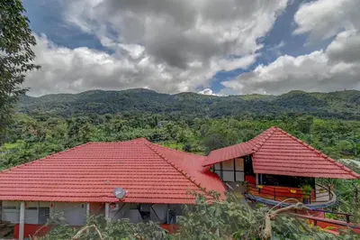 a house with a red roof with mountains in the background at Coorg Heritage Hill View By The Avyaan in Madikeri