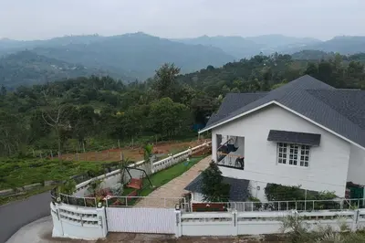 a white house with a balcony and mountains in the background at StayVista at Aashirwaad Villa in Coonoor