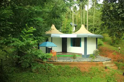 a small house with a blue umbrella in a forest at Vintage Garden Resort in Sultan Bathery