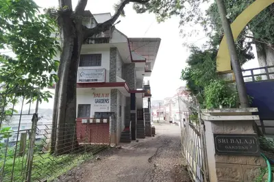 a building on the side of a street with a tree at Ganga's Sri Balaji Cottage in Ooty