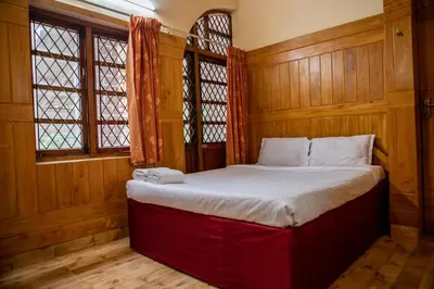 a bed in a room with wooden walls and windows at JJS Cottages in Coonoor
